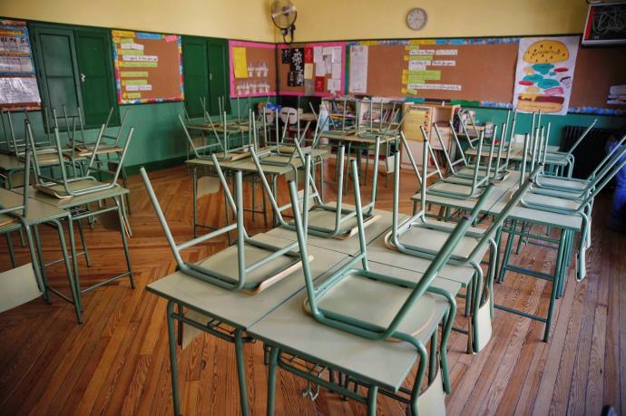 Aula de colegio sin alumnos en la que aparecen las sillas recogidas encima de las mesas